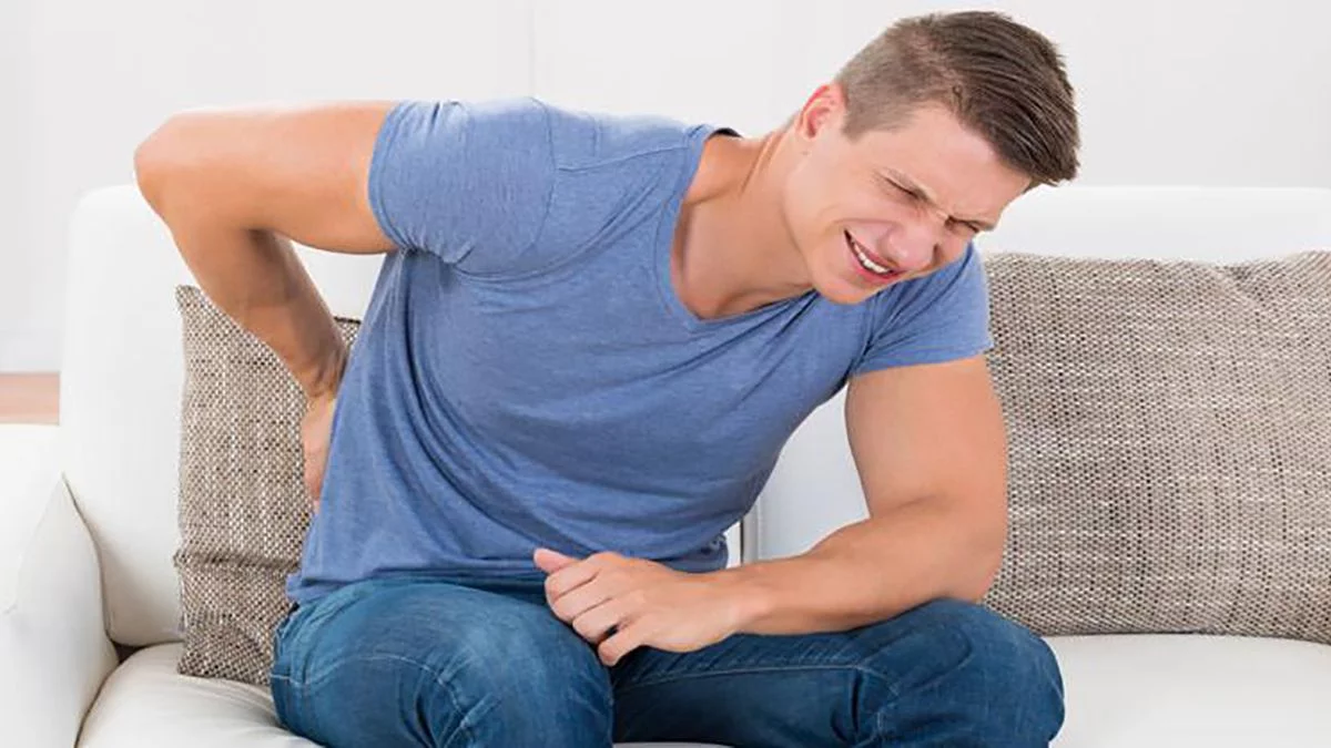 Hombre mostrando signos de dolor en el coxis al levantarse de una silla.